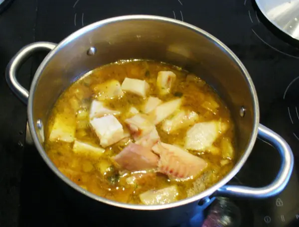 Ein Kochtopf mit einem bunten Fischtopf, der auf einem Herd köchelt, umgeben von einer modernen Küche.