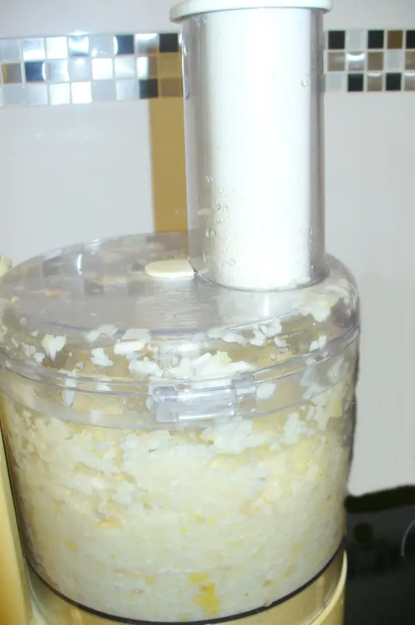 Ein Küchengerät zerkleinert Knoblauch und Zitronen in einem transparenten Behälter auf einer Arbeitsplatte in einer modernen Küche.