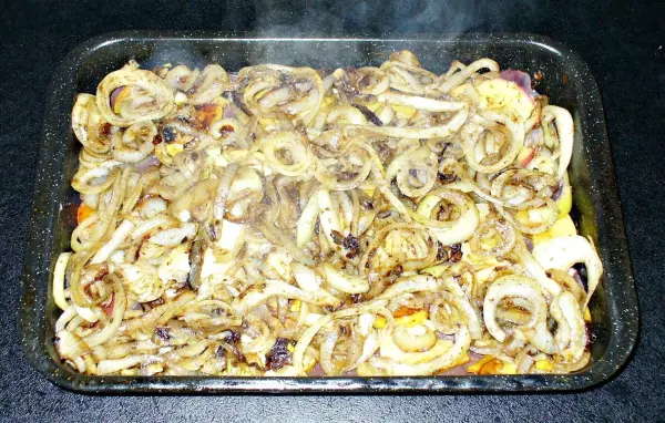 Zarte Leberstücke sind im Backofen zubereitet und dampfen in einer Auflaufform, umgeben von Zwiebelringen und Gewürzen.