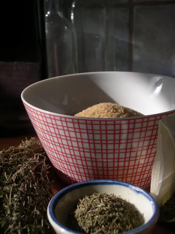 Eine Schüssel mit trockenem Thymian steht im Vordergrund, während aromatische Gewürze in einer Küche sorgsam arrangiert sind.