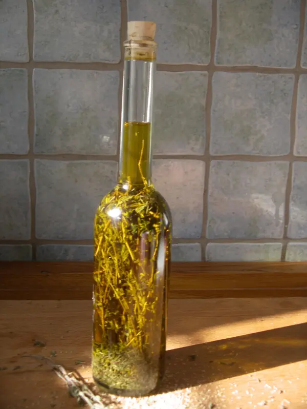 Ein Glasflasche mit grünem Öl ist gefüllt mit frischen Thymianzweigen, steht auf einer Holzoberfläche in einer hellen Umgebung.