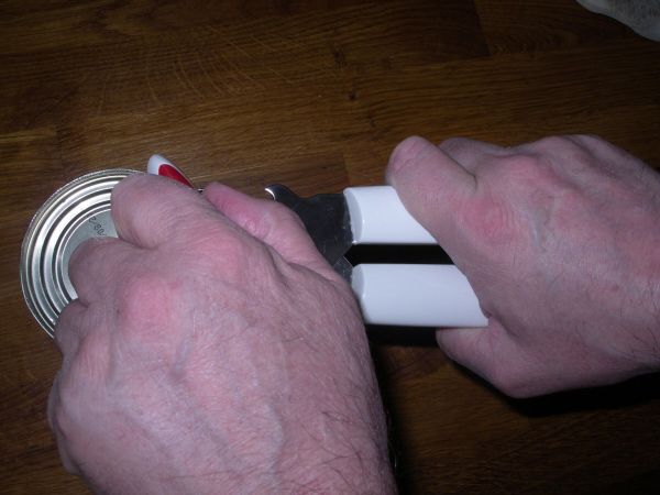 Eine Person benutzt einen Dosenöffner, um eine Dose zu öffnen, während sie gleichzeitig einen sicheren Griff hat.