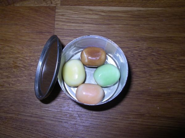 Eine geöffnete Dose zeigt vier bunte Süßigkeiten im Inneren, auf einem Holztisch platziert, bereit zum Verzehr.