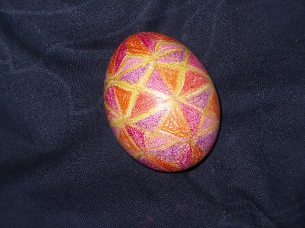 Ein bunt bemaltes Osterei mit geometrischem Muster liegt auf dunklem Stoff.