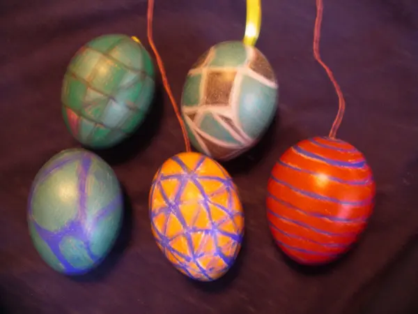 Bunte Ostereier hängen dekorativ auf einem dunklen Hintergrund, jede mit einzigartigen Mustern verziert, die fröhliche Ostern ansprechen.