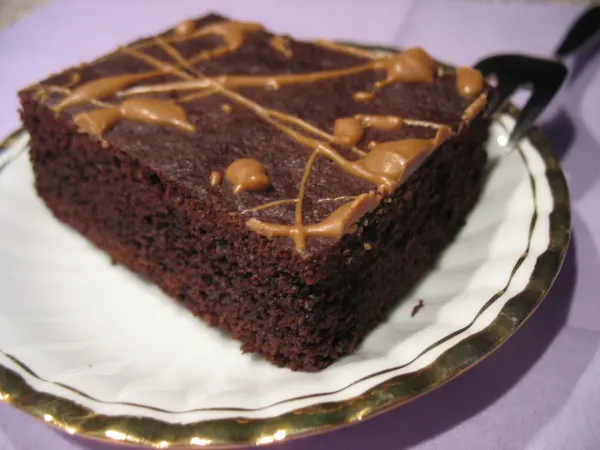 Ein saftiger Brownie liegt auf einem weißen Teller mit goldener Umrandung, umgeben von einem lilafarbenen Tisch.