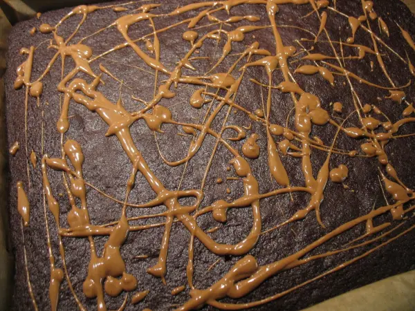 Auf der Oberfläche von geschmolzenen Brownies verläuft schokoladige Karamellsauce in unregelmäßigen Linien.