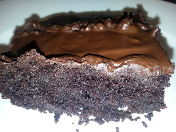 Ein saftiger Brownie liegt auf einem Teller, mit einer glänzenden Schokoladenglasur oben drauf, appetitlich angerichtet.