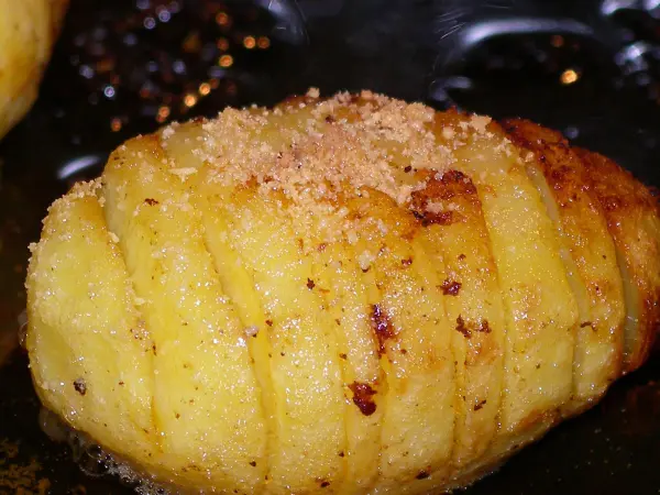 Köstliche Hasselbackspotatis mit goldbrauner Kruste, saftig gebraten, liegt stilvoll auf einem dunklen Teller.
