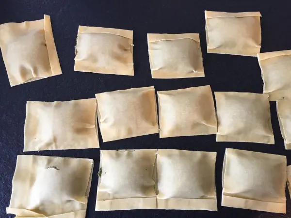 Rechteckige Maultaschen liegen roh und ungekocht auf einer dunklen Fläche, sorgfältig in Reihen angeordnet.