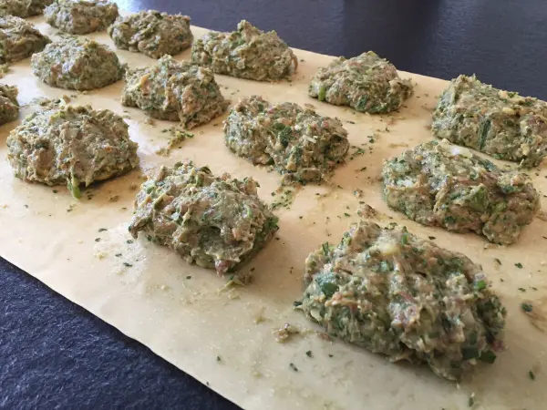 Auf einem Teigblatt liegen mehrere Portionen grüner Maultaschenfüllung, bereit zum Falten und Kochen in einer Küchenumgebung.