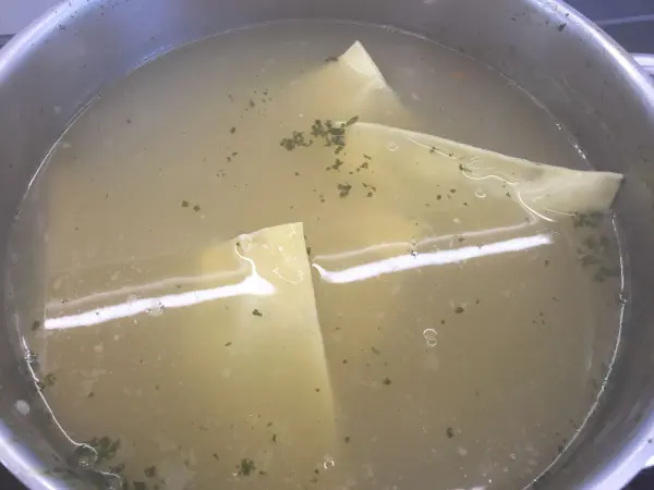 In einem Topf schwimmen Maultaschen in klarer Brühe, garniert mit etwas Kräutern, bereit zum Servieren.