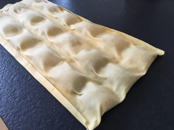Maultaschen-Teig liegt ausgerollt auf einer dunklen Arbeitsfläche, bereit zum Füllen und Schneiden.