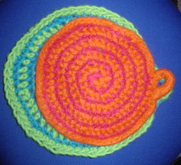 Gefilzte Topflappen in zwei bunten Spiralen liegen auf einem blauen Untergrund und verleihen einen fröhlichen Akzent.