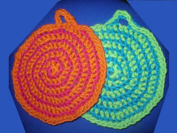 Zweifarbige Topflappen liegen nebeneinander, während sie farbenfroh in Orange und Grün gehäkelt sind.