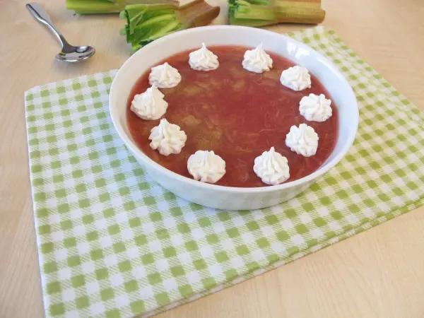 Eine Schüssel Rhabarbergrütze, dekoriert mit Sahnehäubchen, liegt auf einem karierten Tischcloth aus Baumwolle.