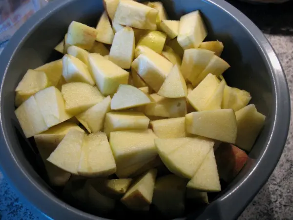 In einer Schüssel liegen frisch geschnittene Äpfel bereit, um für einen Apfelkuchen mit Dinkelmehl verwendet zu werden.