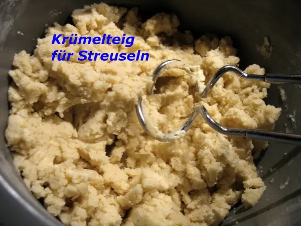 Krumeliger Streuselteig wird mit Rührbesen in einer Schüssel zubereitet, bereit für den Apfelkuchen mit Dinkelmehl.