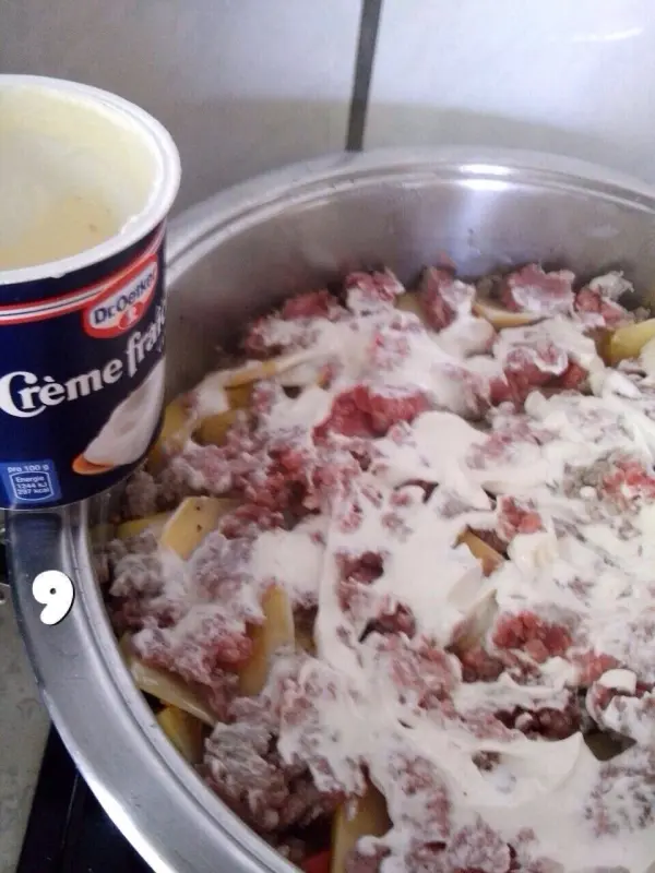 Eine große Pfanne enthält Kohlrouladen, gemischt mit Hackfleisch und überzogen mit einer cremigen Sauce, bereit zum Kochen.