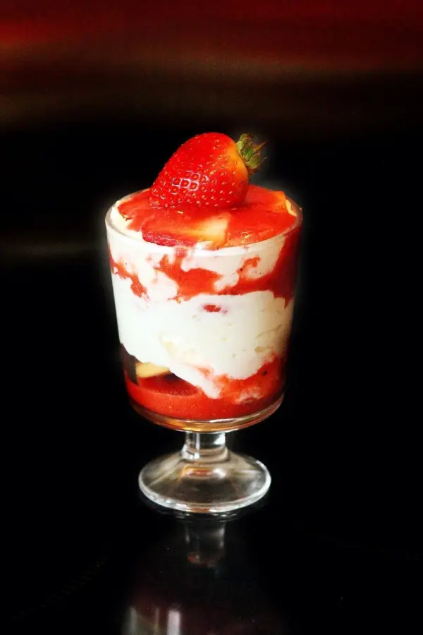 Ein Glas mit Erdbeer Tiramisu zeigt geschichtete Mascarpone-Creme und Erdbeeren, gekrönt von einer frischen Erdbeere.