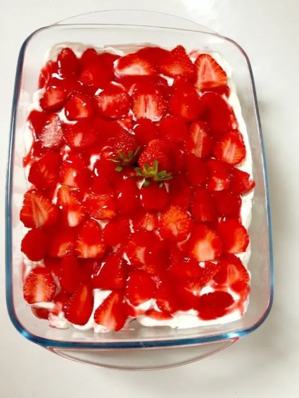 In einer rechteckigen Glasschüssel liegen frisch geschnittene Erdbeeren auf einer Schicht Mascarponecreme.