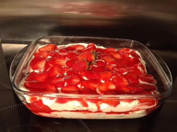 Erdbeer-Tiramisu füllt eine rechteckige Glasform. Frische Erdbeerscheiben bedecken eine Schicht aus cremiger Mascarpone.