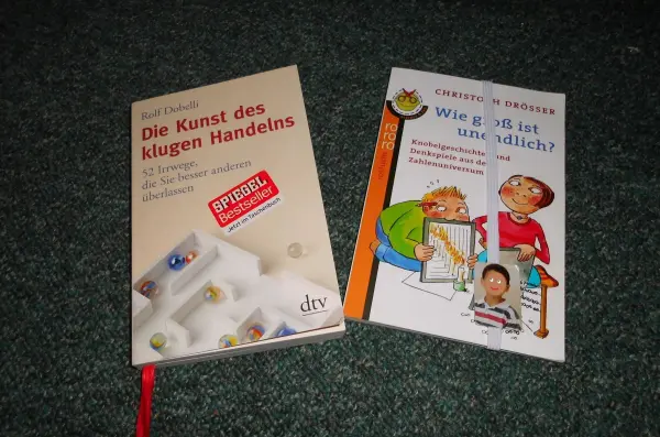 Bücher mit Lesebändchen liegen auf einem dunklen Teppich, eins zeigt Anleitungen, das andere illustriert Kinderaktivitäten.