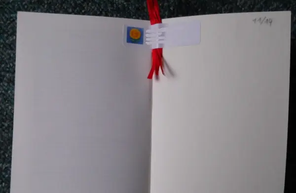 Ein personalisiertes Lesebändchen mit roter Schleife und einem Platz für Foto oder Namen ist in einem offenen Buch zu sehen.