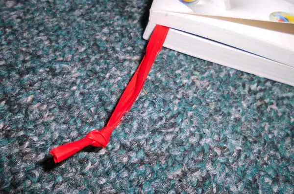 Ein rotes Lesebändchen liegt an einem Buch, das offen auf einem Teppich liegt, bereit zum Blättern.