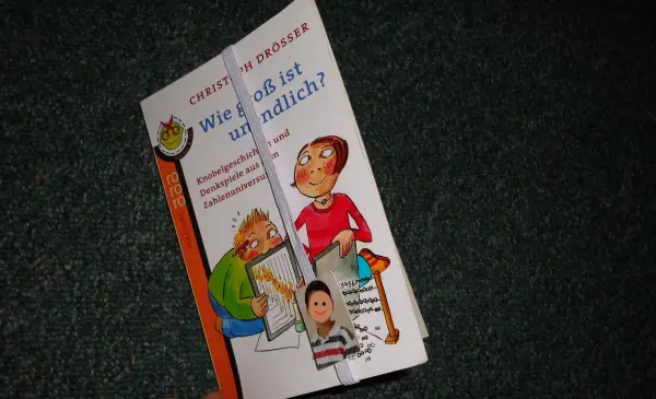 Ein farbenfrohes Lesebändchen mit einem Foto, das ein Buch hält und den Titel "Wie geht es eigentlich?" zeigt.
