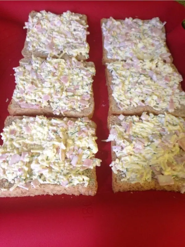 Sechs Brotscheiben mit einer üppigen Mischung aus Schinken und Käse belegt, auf einem roten Untergrund vorbereitet.