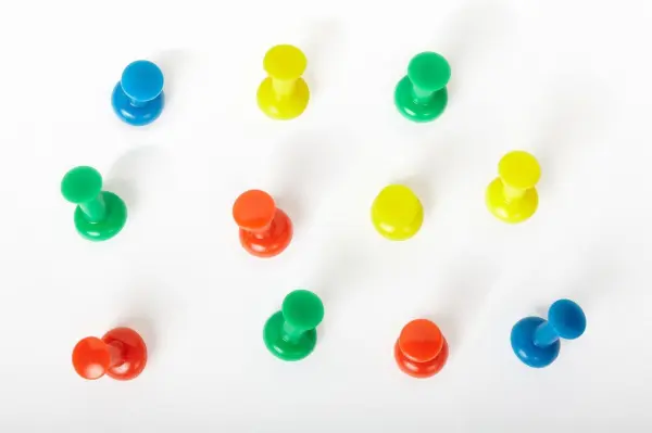 Bunte Reißnägel liegen verstreut auf einer weißen Fläche, bereit zum Befestigen von Notizen an der Wand.