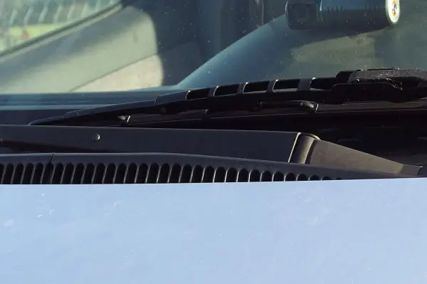 Ein Scheibenwischer bewegt sich über die B-Seite einer Windschutzscheibe in einem Fahrzeug, während die Sonne scheint.