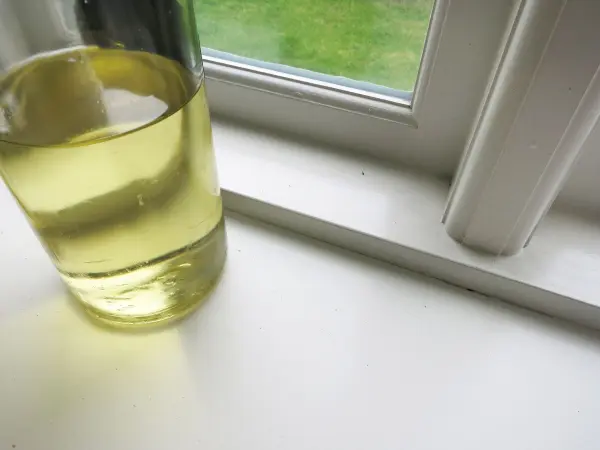 Ein Glas mit Speiseöl steht neben einem weißen Fensterrahmen, wo es verwendet wird, um weiße Fugen zu reinigen.