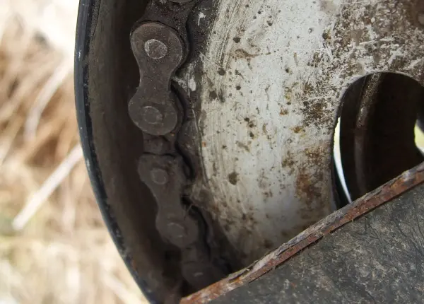 Eine verschmutzte Kette an einem Rad dreht sich schwerfällig in einer staubigen Umgebung, überzogen mit schwarzem Fett.