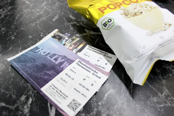 Zwei Kinotickets liegen neben einem geöffneten Beutel Popcorn auf einem Tisch vor einem Filmstart.