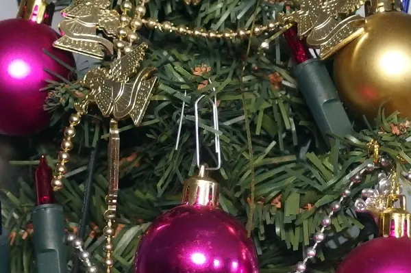 Bunte Weihnachtskugeln hängen an einem Tannenbaum, gesichert mit Büroklammern, um eine festliche Atmosphäre zu schaffen.