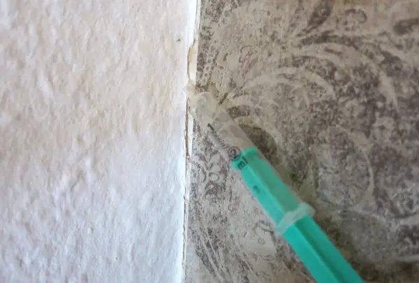 Eine grüne Spritze zeigt eine lockere Stelle in der Tapete, die Beulen aufweist, an einer Wand zwischen zwei Oberflächen.