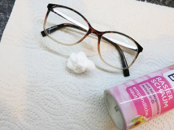 Eine Brille liegt auf einem Küchenpapier, während daneben Rasiergel platziert ist, bereit zum Reinigen der Gläser.