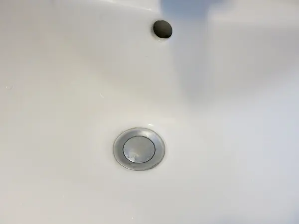 Waschbeckenstöpsel sitzt fest in einem weißen Waschbecken, umgeben von glatter Keramikoberfläche ohne sichtbares Wasser.