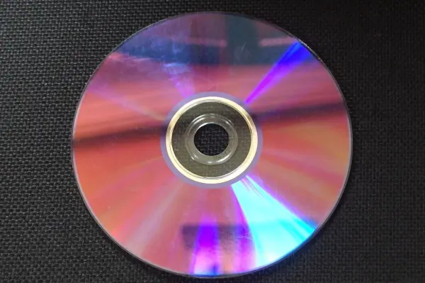 Eine CD mit Kratzern liegt auf einer dunklen Oberfläche, bereit, mit Autopolitur gereinigt zu werden.