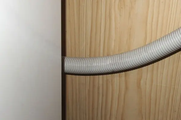 Eine Waschmaschine mit einem grauen Ablaufschlauch, der hinter einem Holzpaneel verläuft, lässt Wasser sofort ablaufen.