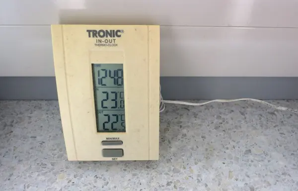Thermo-Uhr zeigt Zeit (12:48), Innentemperatur (23,8°C) und Außentemperatur (22,9°C) an, kabelgebunden auf grauem Boden.