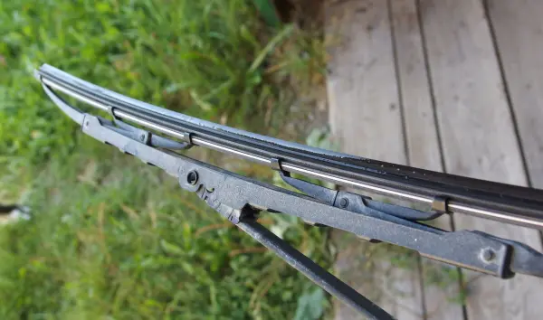 Ein Scheibenwischer mit Gummiblatt, das in einem grünen Umfeld auf einem Holzdeck steht, wird sichtbar gepflegt.