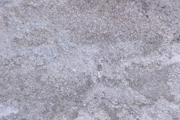 Der lose Putz hat sich an der Wand gelöst, während der graue Untergrund uneben und strukturiert aussieht.