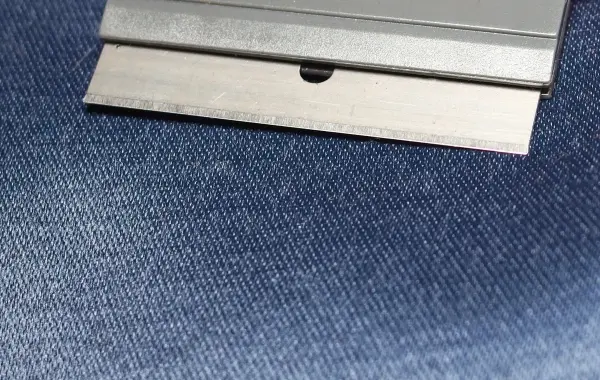 Eine Rasierklinge liegt auf einem blauen Stoff, bereit zur Reinigung, während sie das Material berührt.