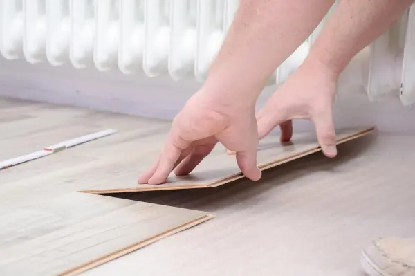 Hände legen ein Klicklaminat-Element auf den Boden, während im Hintergrund ein Heizkörper zu sehen ist.