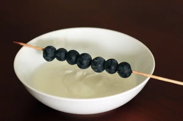 Ein Spieß mit Heidelbeeren schwebt über einer Schale mit Joghurt, bereit zum Eintauchen und Genießen.