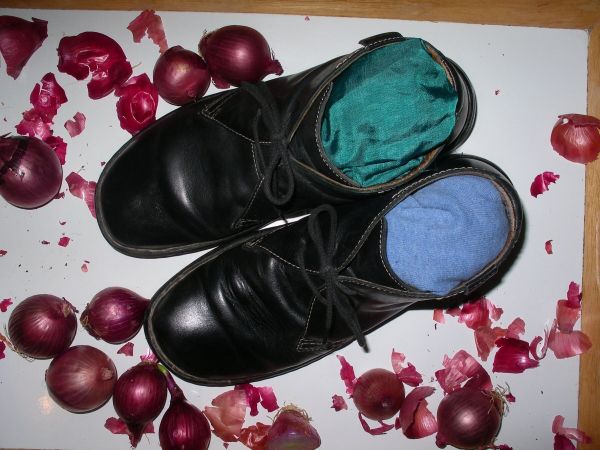 Schwarze Glattlederschuhe liegen auf einem Untergrund, gefüllt mit bunten Socken, um sie zu formen, umgeben von roten Blütenblättern.
