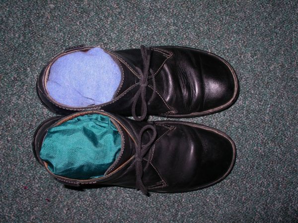 Schwarze Glattleder Schuhe zeigen die Innenseiten mit blauen und grünen Einlagen auf einem Teppich.